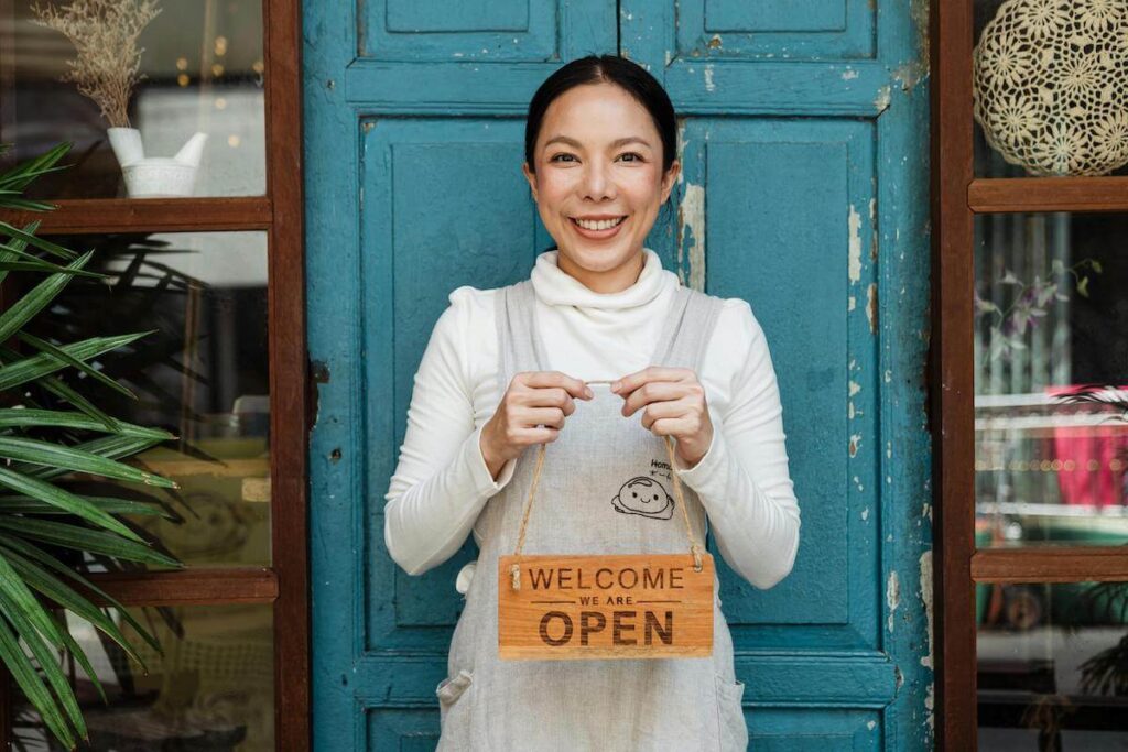 Smiling woman business owner holding a 'Welcome, We Are Open' sign, showcasing success with Marin Google Maps Marketing.