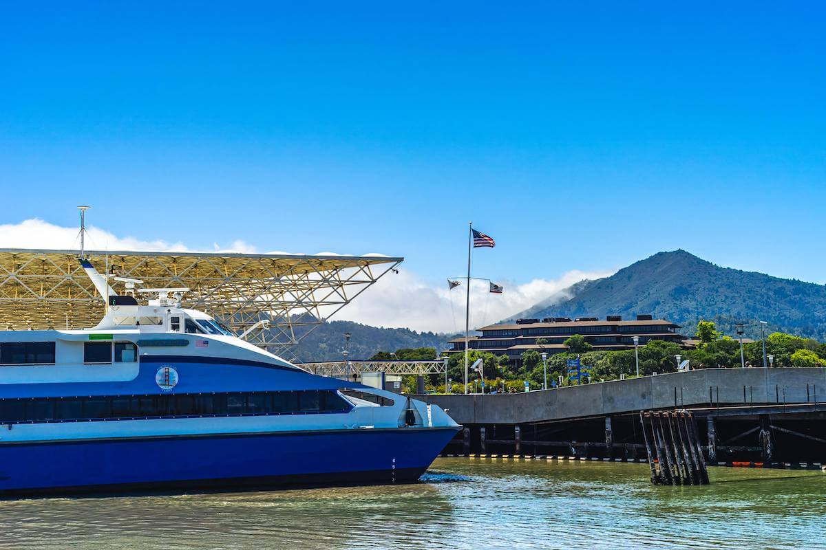 A ferry boat in the bay near Larkspur Harbor, Marin County, preparing to pick up passengers with an American flag in the distance.