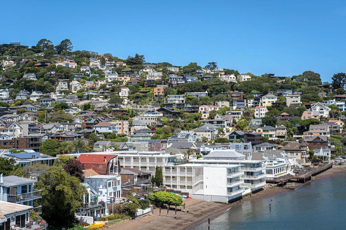A sunny view of Sausalito, Marin County, featuring hillside homes overlooking a beach with a bright blue sky.
