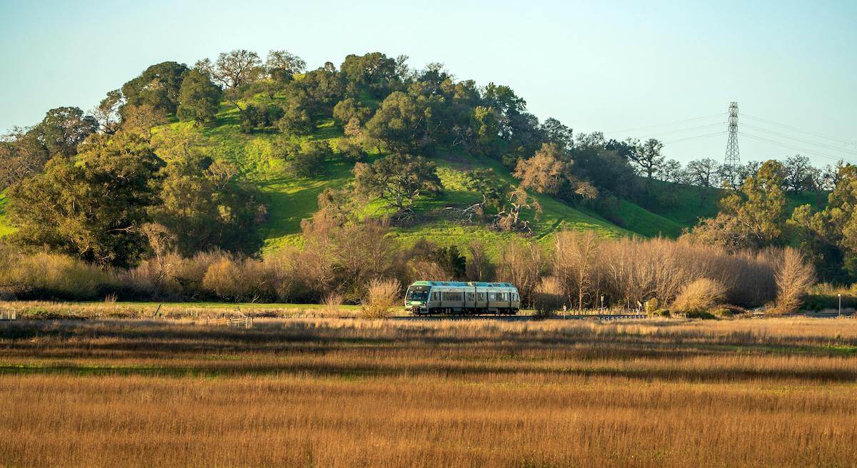 A SMART Train crossing the open landscape in San Rafael, Marin County, with rolling hills in the background.