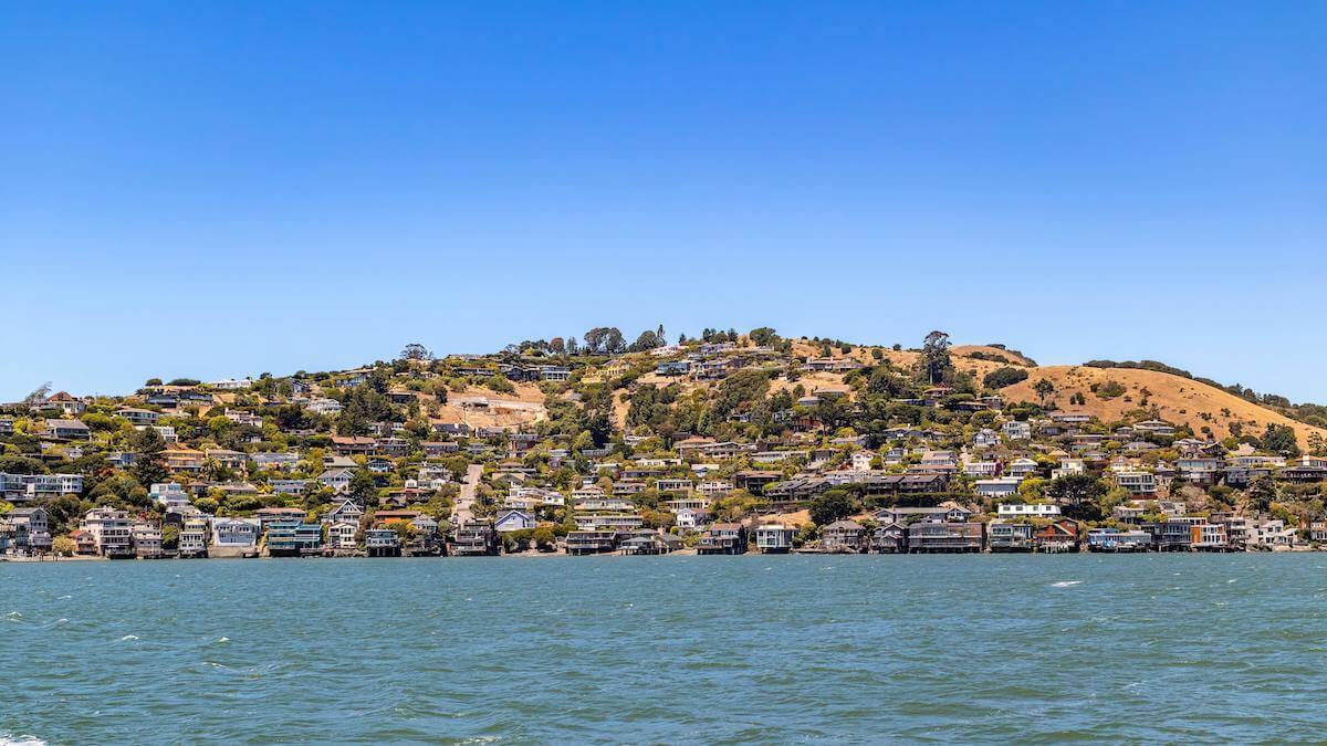 A scenic view from the Bay looking at coastal homes in Tiburon, Marin County, under a bright blue sky.
